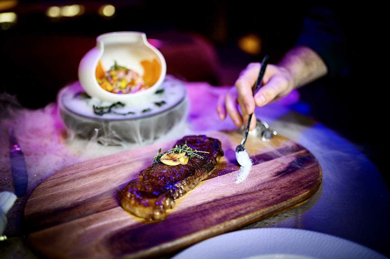 steak on a wooden platter with other food dishes in the background